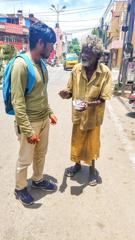 A Rotaractor gives a meal packet to a street dweller.
